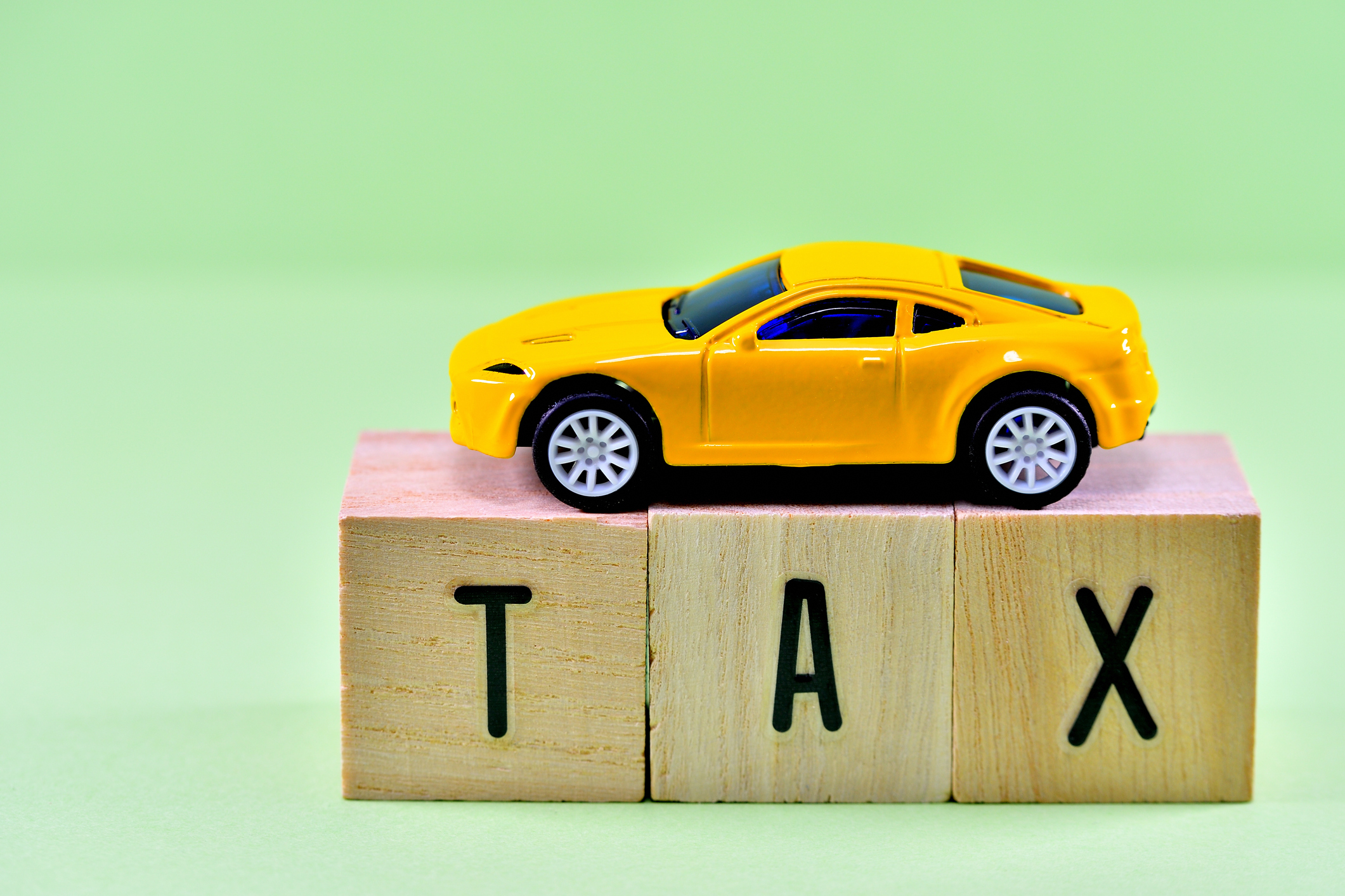 yellow car on top of the word &quot;tax&quot; spelled out in wooden blocks