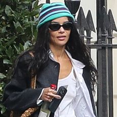 Zoe kravitz wears a stripe hat, black jacket, and a white tee with a button-down shirt.