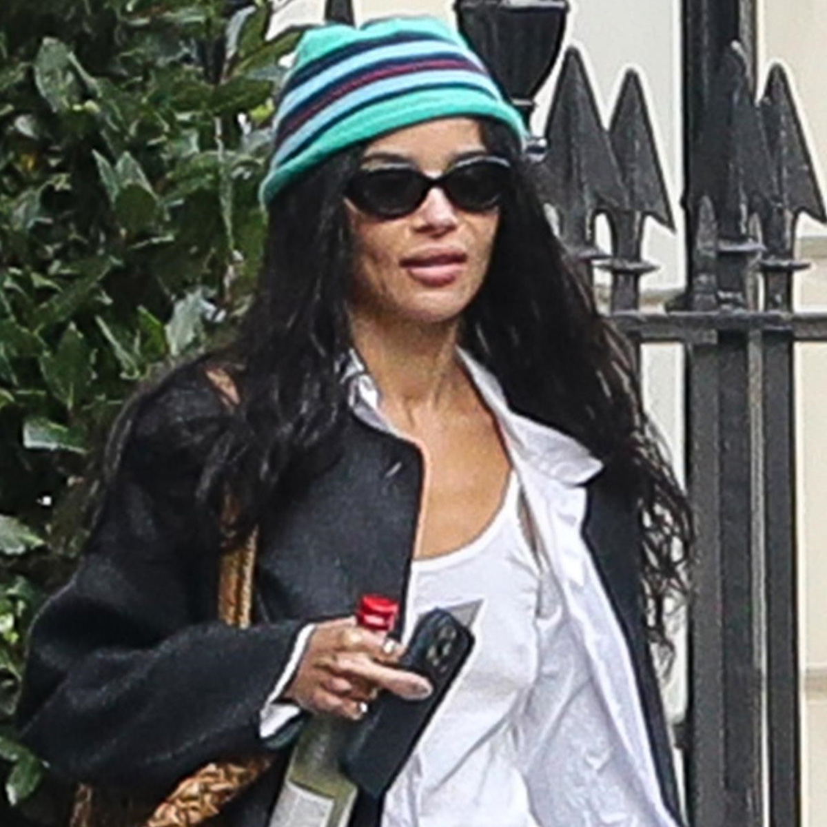Zoe kravitz wears a stripe hat, black jacket, and a white tee with a button-down shirt.