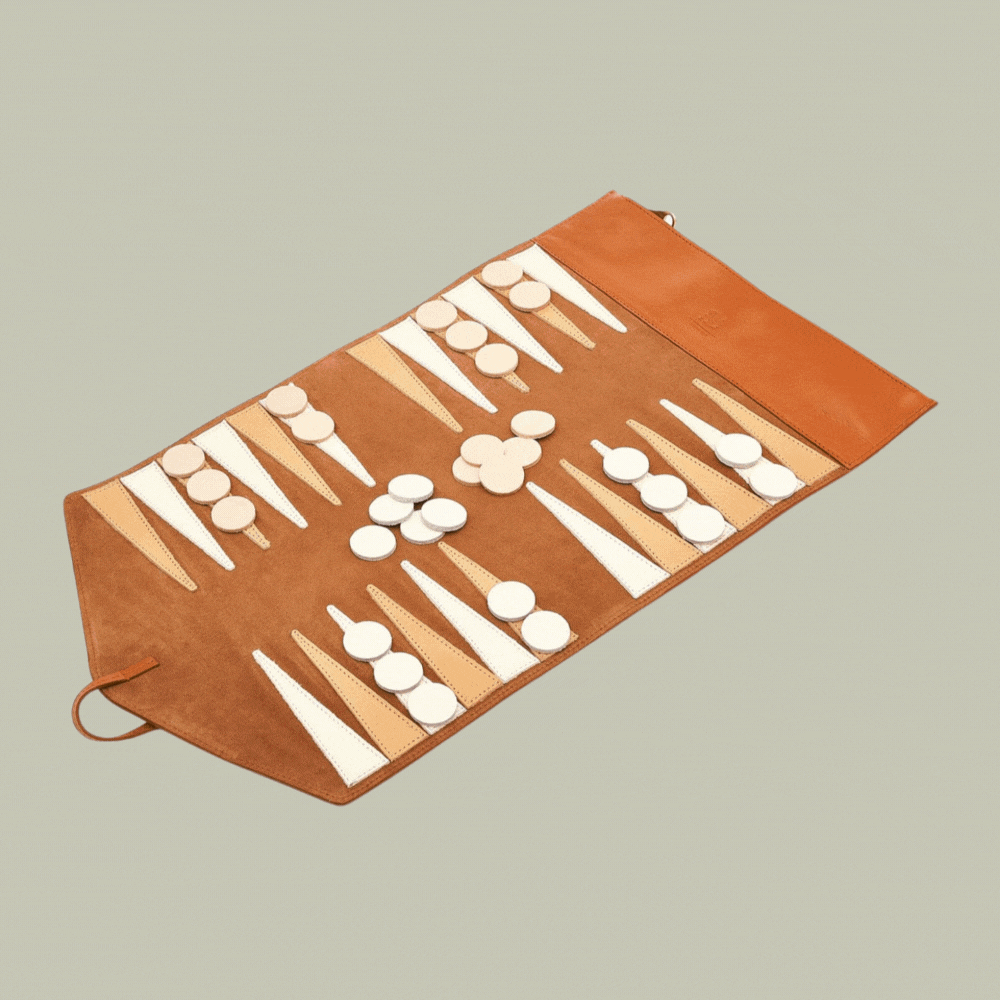 Il Bisonte Caramel Leather Travel Backgammon Set in a rotating gif that shows it open against a pale green background and placed on a wooden table.