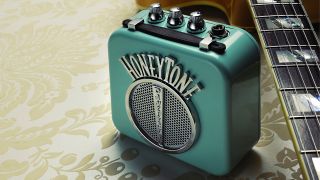 A Danelectro Honeytone mini amp on the floor with a guitar lying next to it