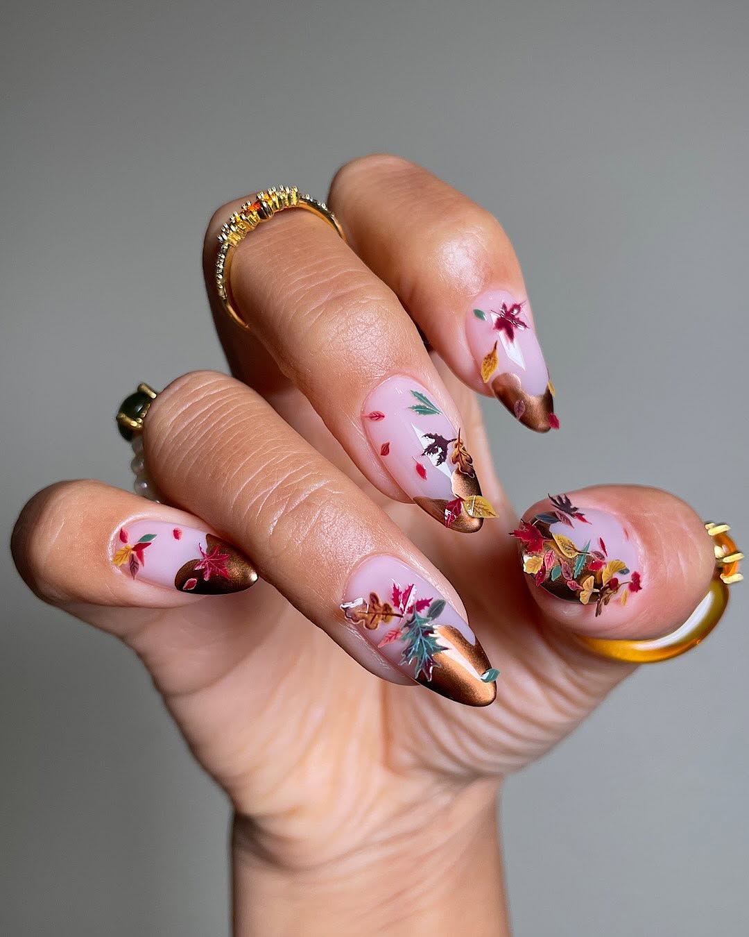 Close-up photo of a person&amp;rsquo;s hand showcasing copper brown tips on almond nails with tiny floral nail stickers.