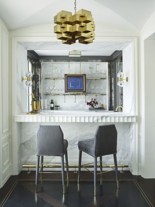 A small home bar, with two bar stools, and a statement light above it