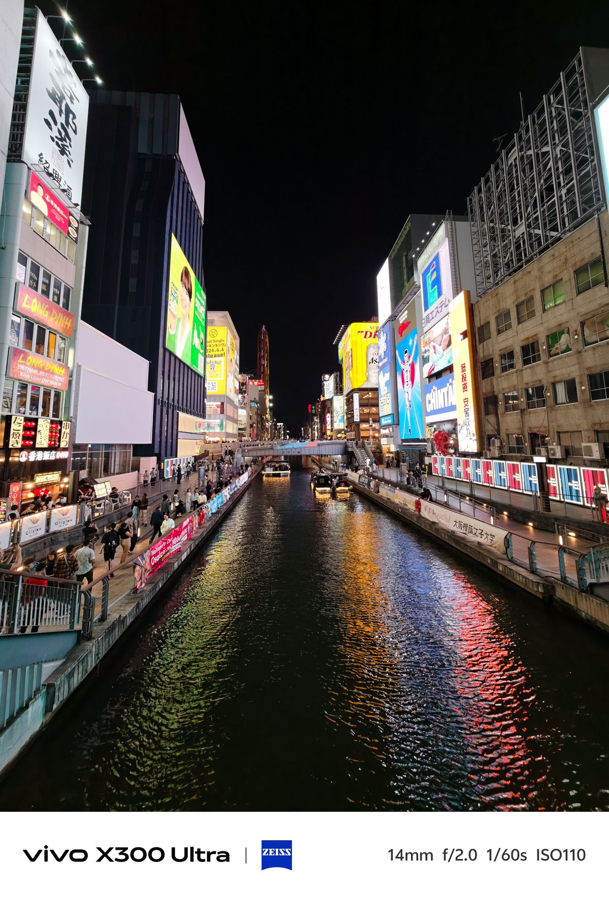 A view down a vibrant city canal lined with bright, colorful neon advertisements and billboards reflecting onto the water.