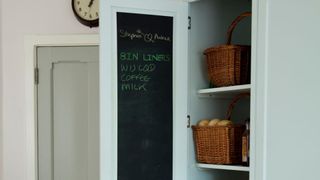 Pale blue kitchen pantry cupboard with chalkboard mounted on the inside of the doors with shopping list