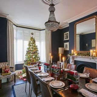 Dining room with dark blue walls with table and chairs with table settings decorated for Christmas