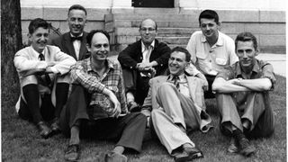 A black and white photo of men smiling and sitting on the grass