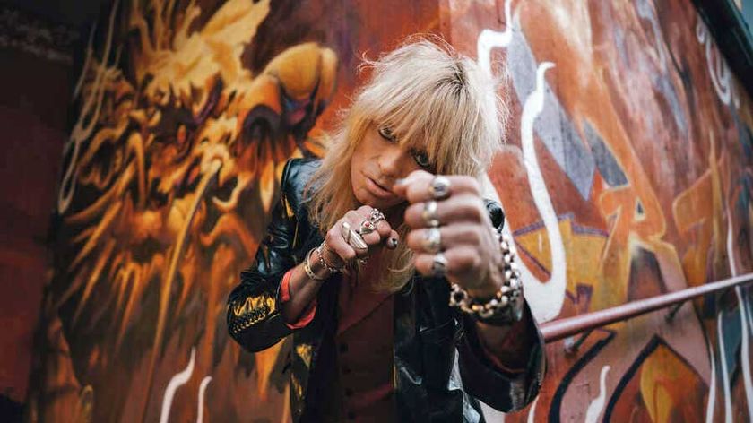 Michael Monroe shadow boxing at the camera in front of a wall covered in graffiti