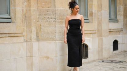 Lena Mahfouf wears gold large earrings, a black embossed striped pattern / shoulder-off / long slit / split dress, black shiny strappy leather small heels sandals , outside the COS show, on April 26, 2023 in Paris, France.