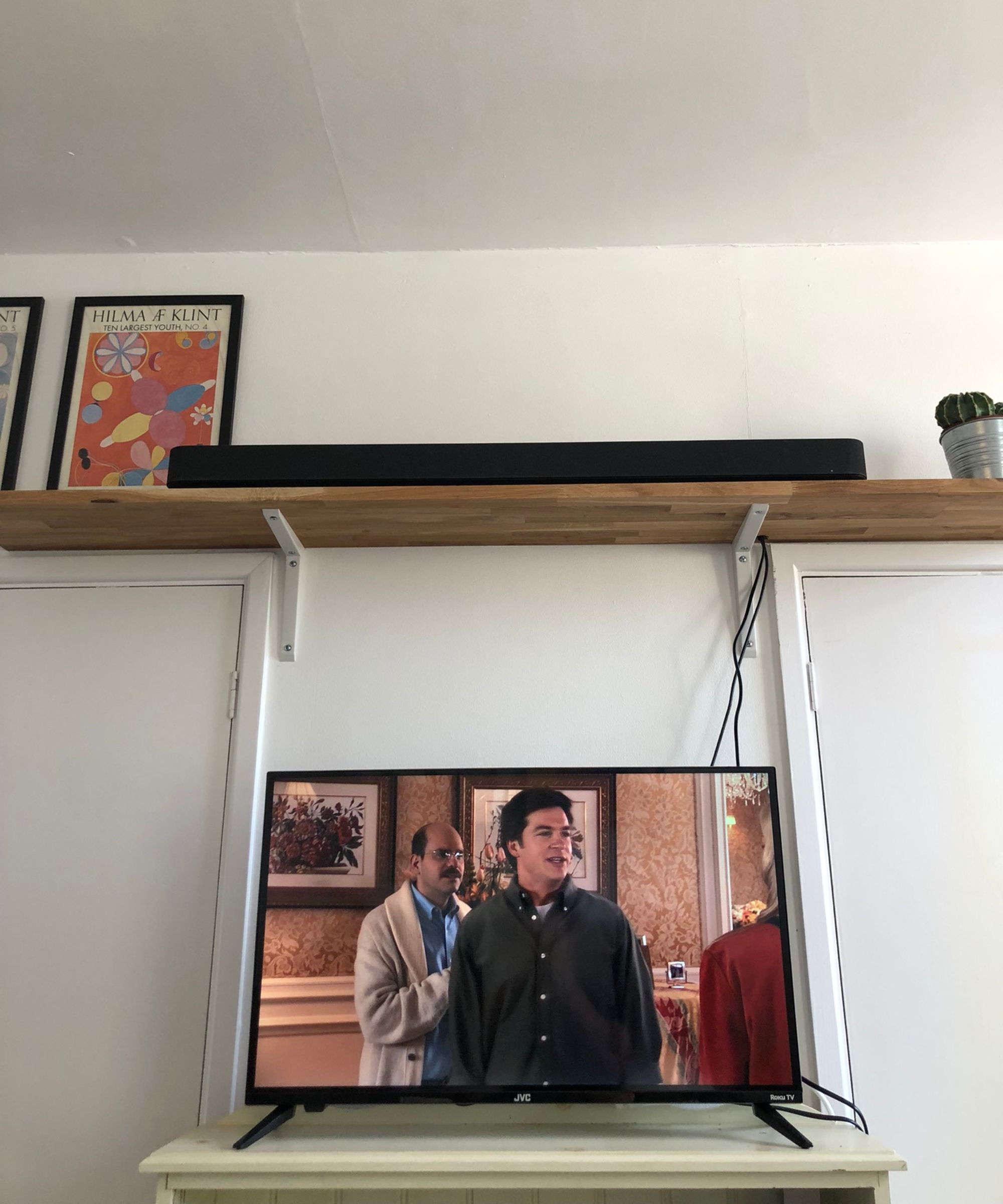 TV showing Arrested Development on bookshelf, with Sony BRAVIA Theater Bar 8 soundbar and cactus above on wooden shelf, next to art prints and against a white wall in Dan Fauzi&#039;s home.