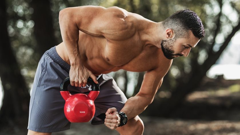 Muscled male rowing kettlebell with right arm outdoors