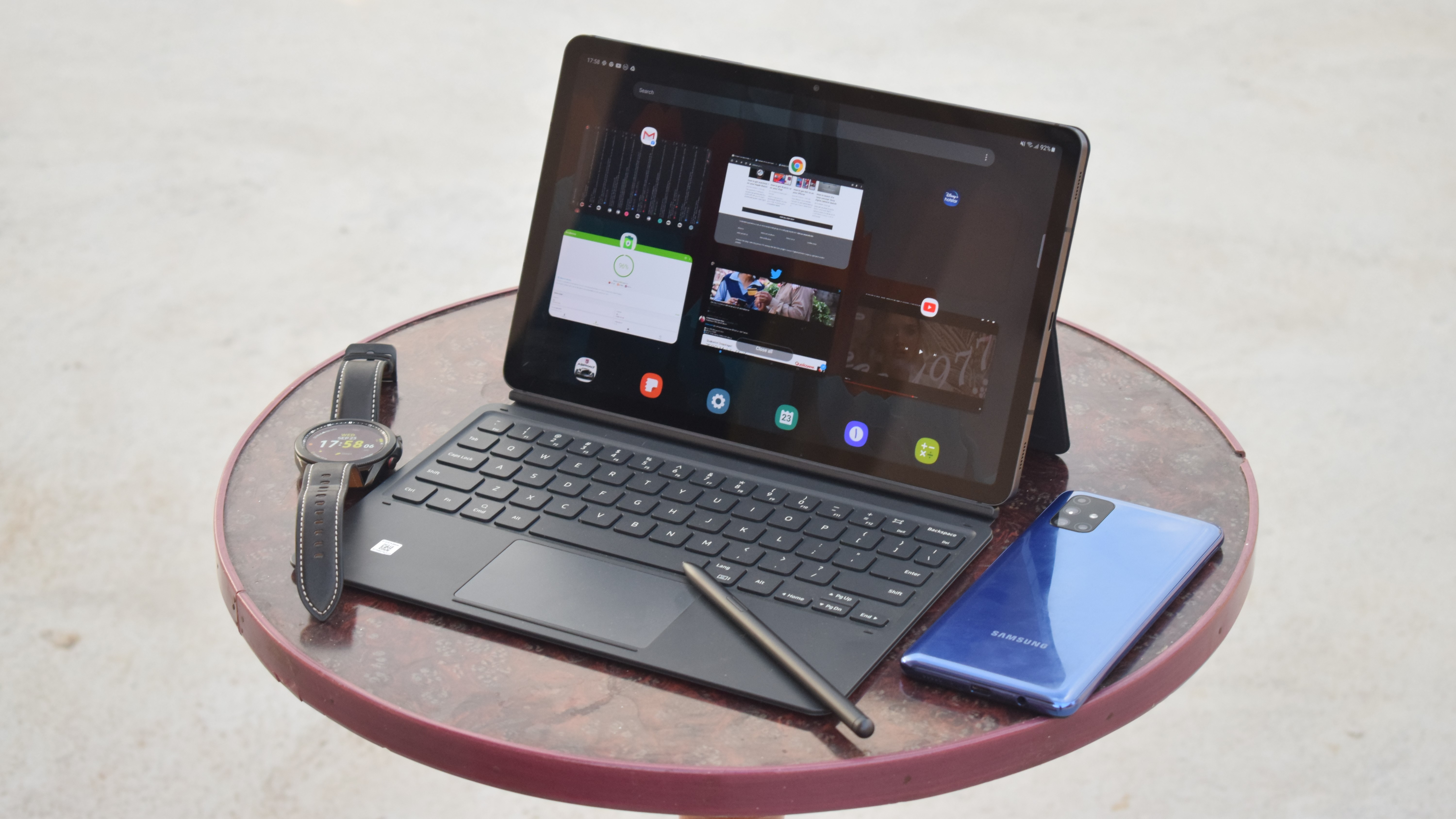 A Samsung Galaxy Tab S7 with a keyboard case, next to a smartwatch and phone