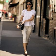 Chic Parisian woman wearing a white top and skirt with black strappy sandals, black bag and black sunglasses