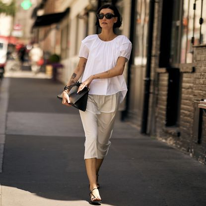 Chic Parisian woman wearing a white top and skirt with black strappy sandals, black bag and black sunglasses