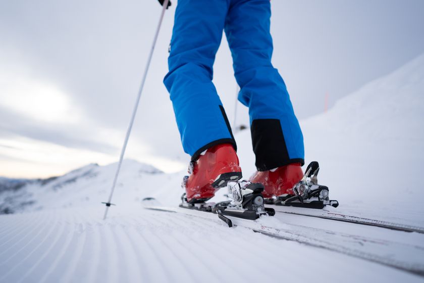 A close up of a skier on the mountain with blue pants and red ski boots