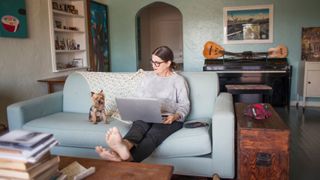Woman sitting at home on the sofa with laptop looking at dog