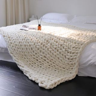 A bedroom with white sheets and a cream chunky knitted throw