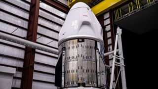 a white conical dragon spacecraft sits in a large room with silver and black walls