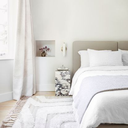 A contemporary bedroom with a marble bedside table and bed dressed in white bedding