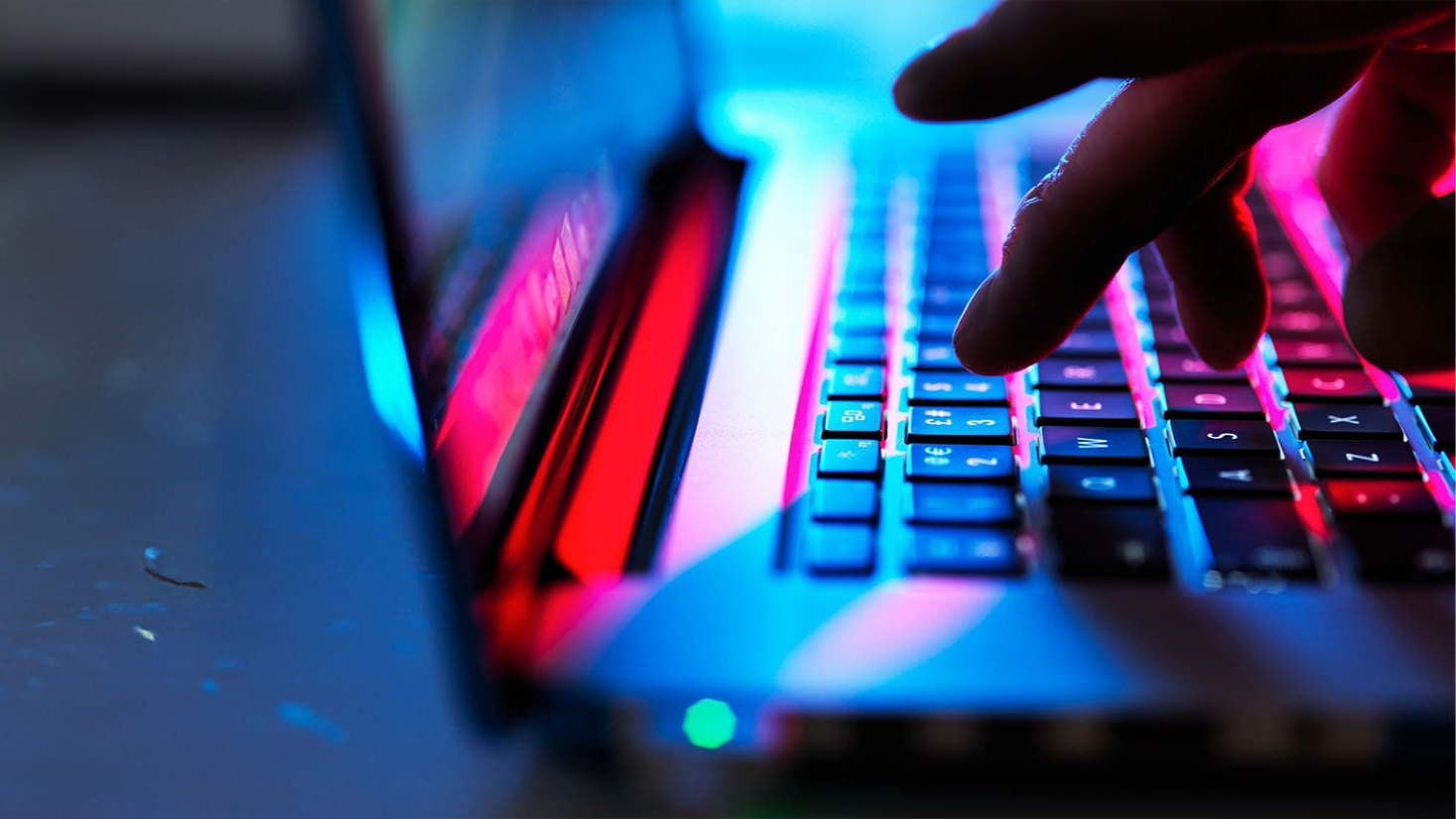 A hand typing on a keyboard in the dark