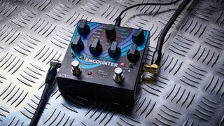 The Source Audio Encounter delay and reverb pedal is photographed here in close-up against an industrial metal background.