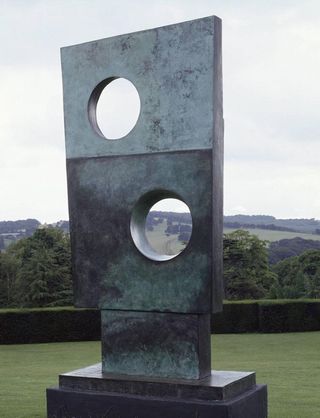 Large rectangular bronze sculpture with round peepholes for viewing the green landscape behind it.