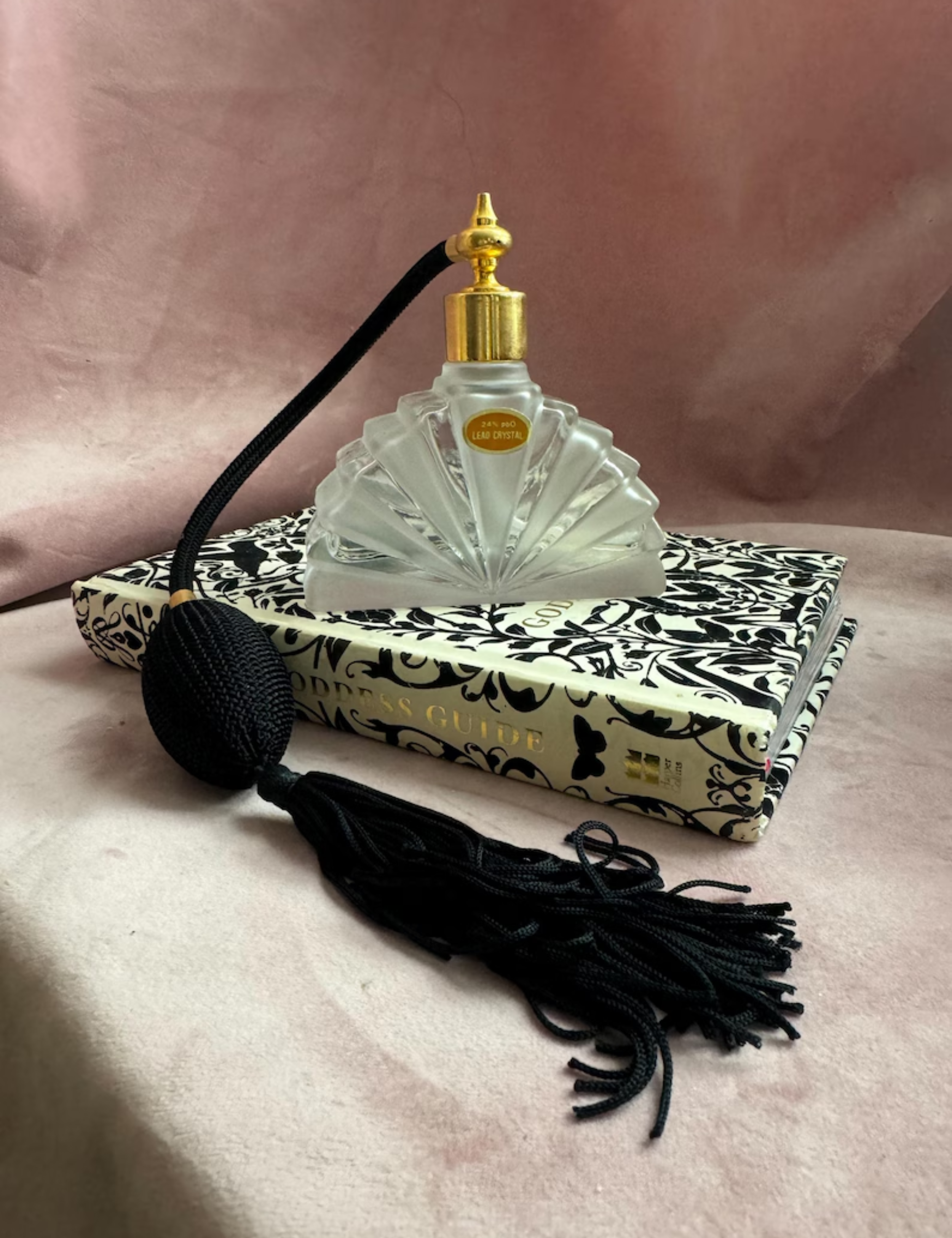 Vintage perfume bottle resting atop of a patterned book