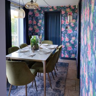 Dining room decorated with pink and blue floral wallpaper with dining table and green chairs