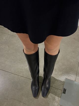 Woman wears black skirt and black knee high boots