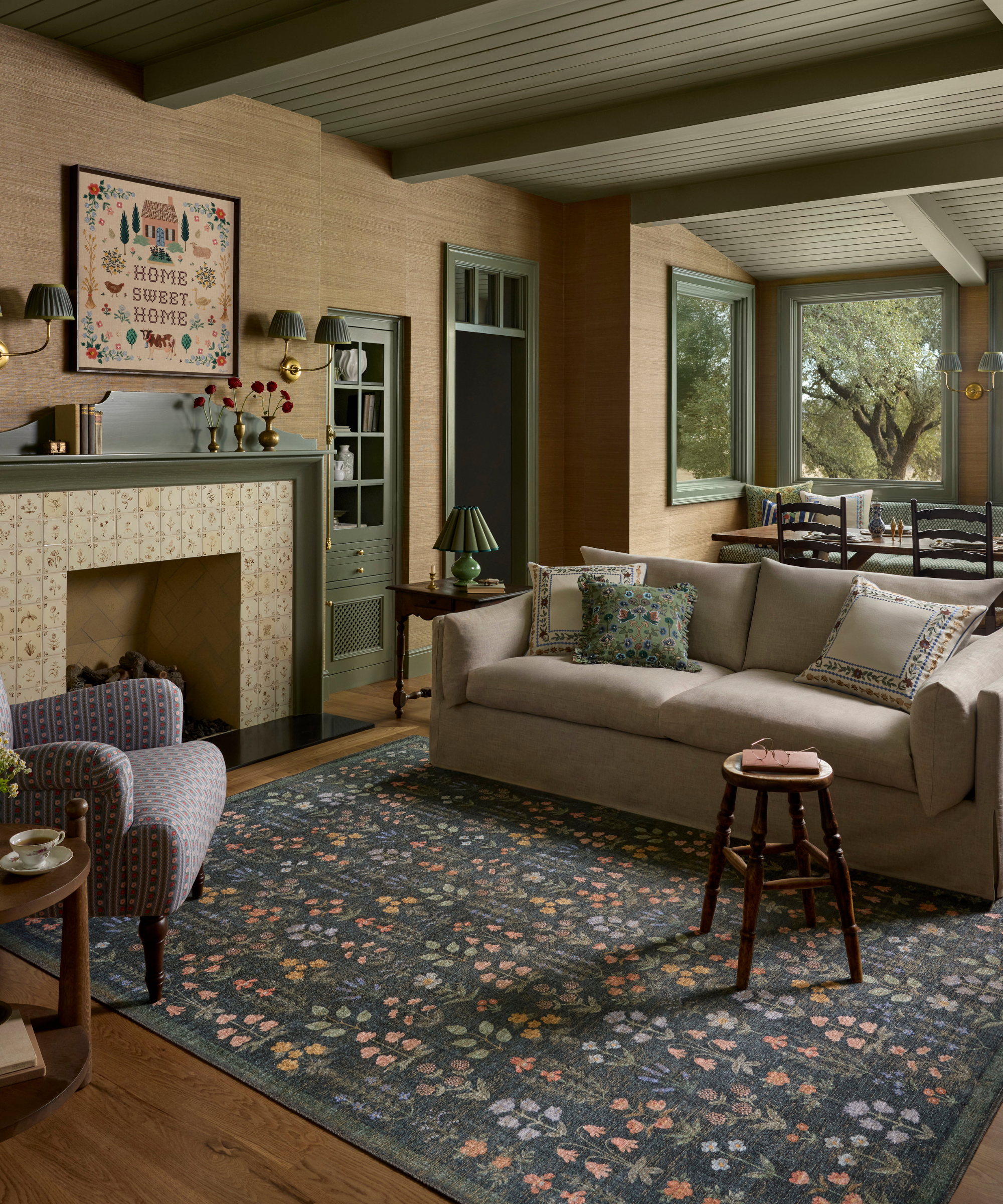 a characterful living room with a floral rug, a tan couch with pillows on it, a tiled fireplace with a 'Home Sweet Home' picture above it, and a green painted ceiling
