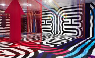 art display in room with black and white patterns on the walls and ground with hanging coloured strings in different shapes