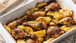 A roasting tin filled with potatoes and herby chicken drumsticks