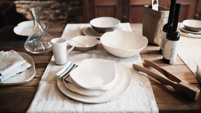 A wooden table laid with white dinnerware and a table runner