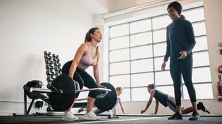 Woman lifting trap bar in gym as instructor looks on