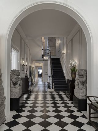 A large entryway with a large staircase and black and white checkerboard flooring