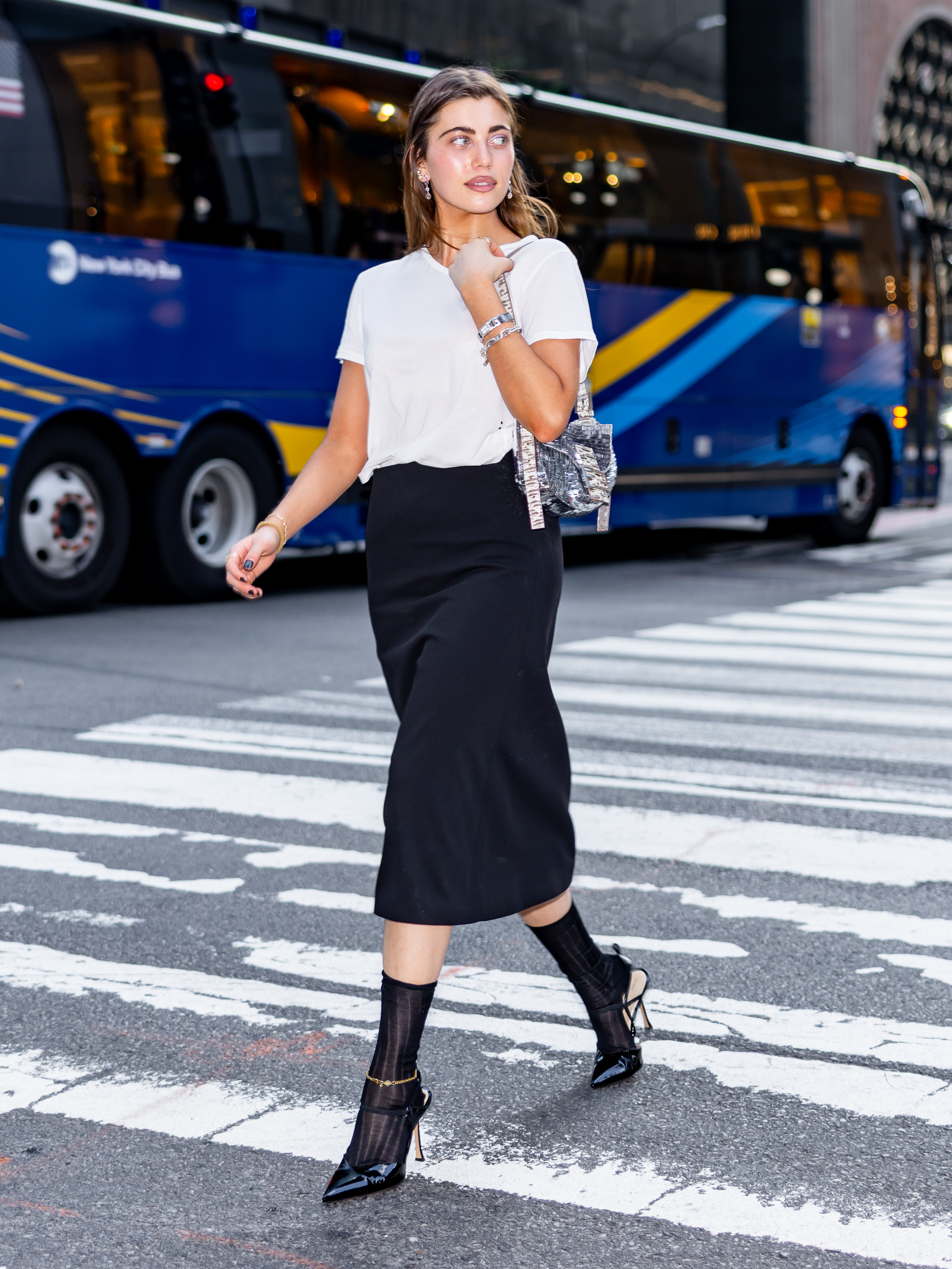 Amelie Zilber walks down the street in New York wearing a black pencil skirt with a t-shirt, heels and sheer socks.