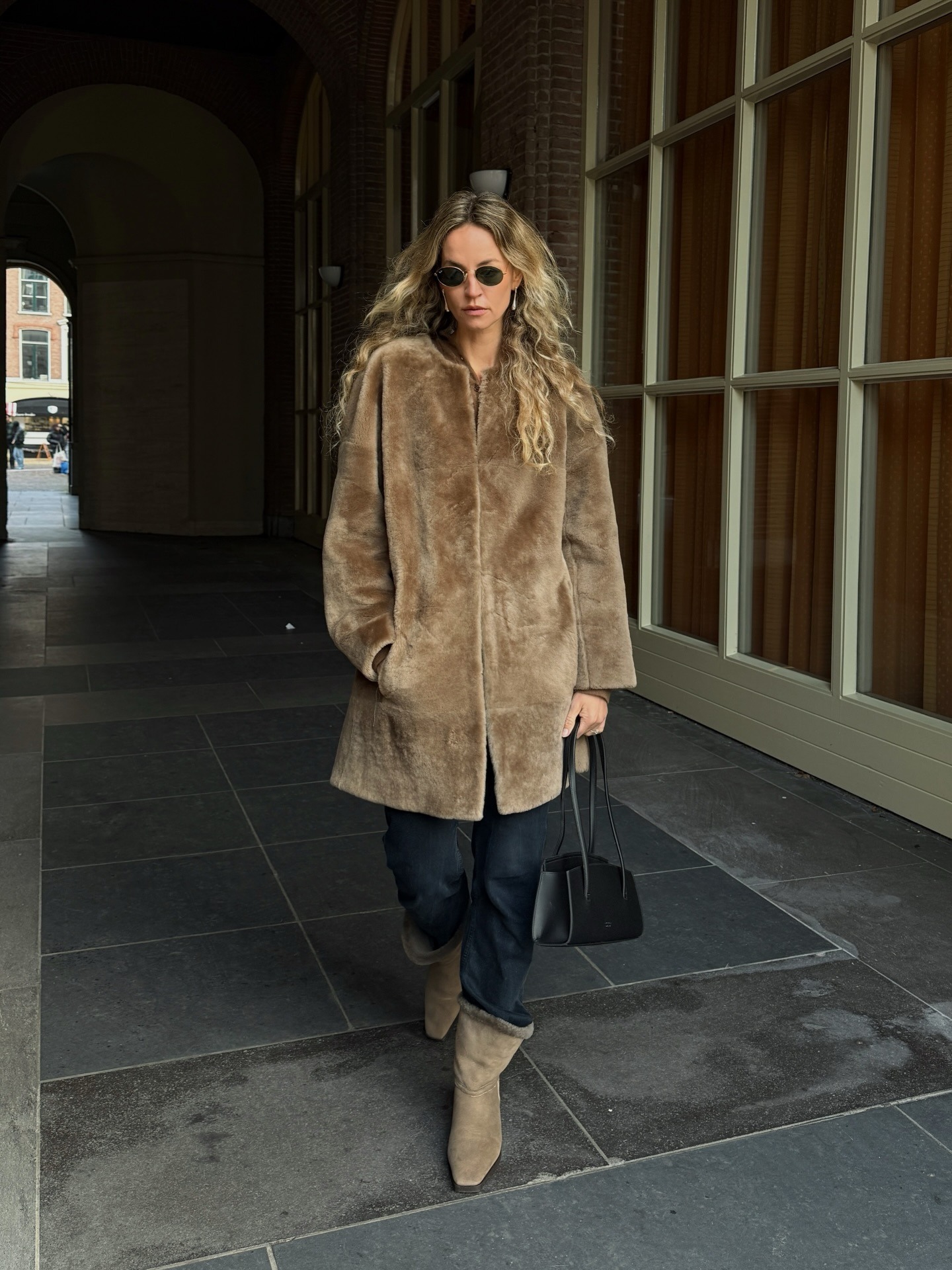 Woman wears Toteme boots, faded black jeans, faux fur coat and structured purse.