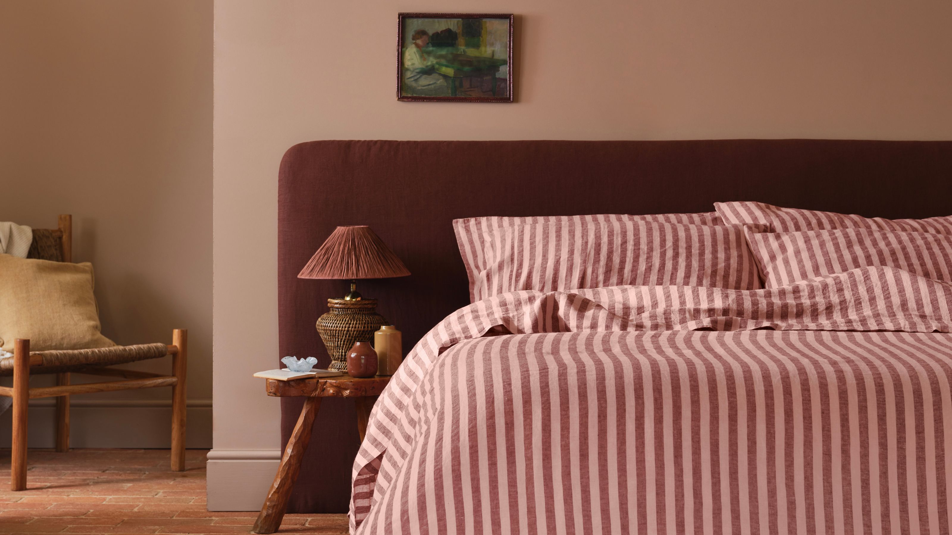 A bedroom with plaster pink walls, jute carpet, and a minimalist bed with pink striped bedding and pillows. 