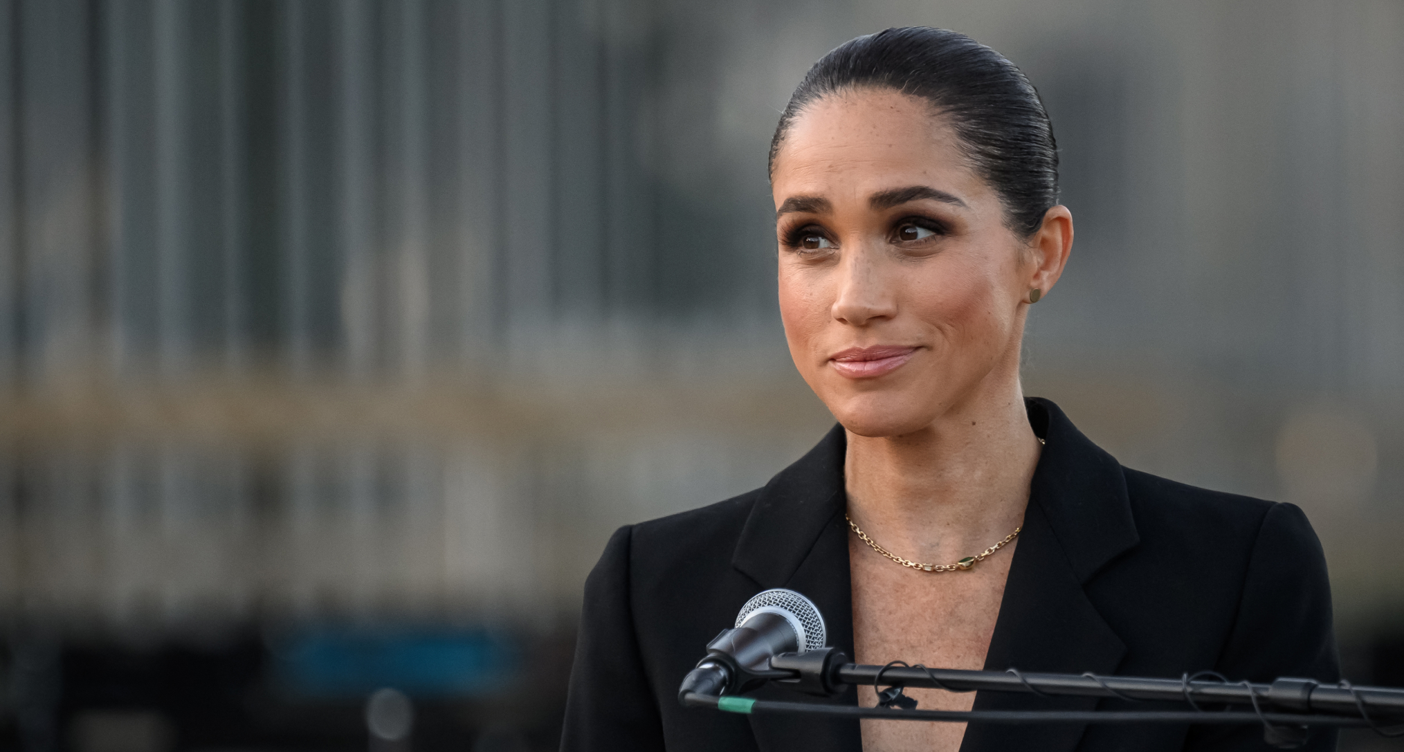 Meghan Markle wearing a black suit giving a speech in a mic