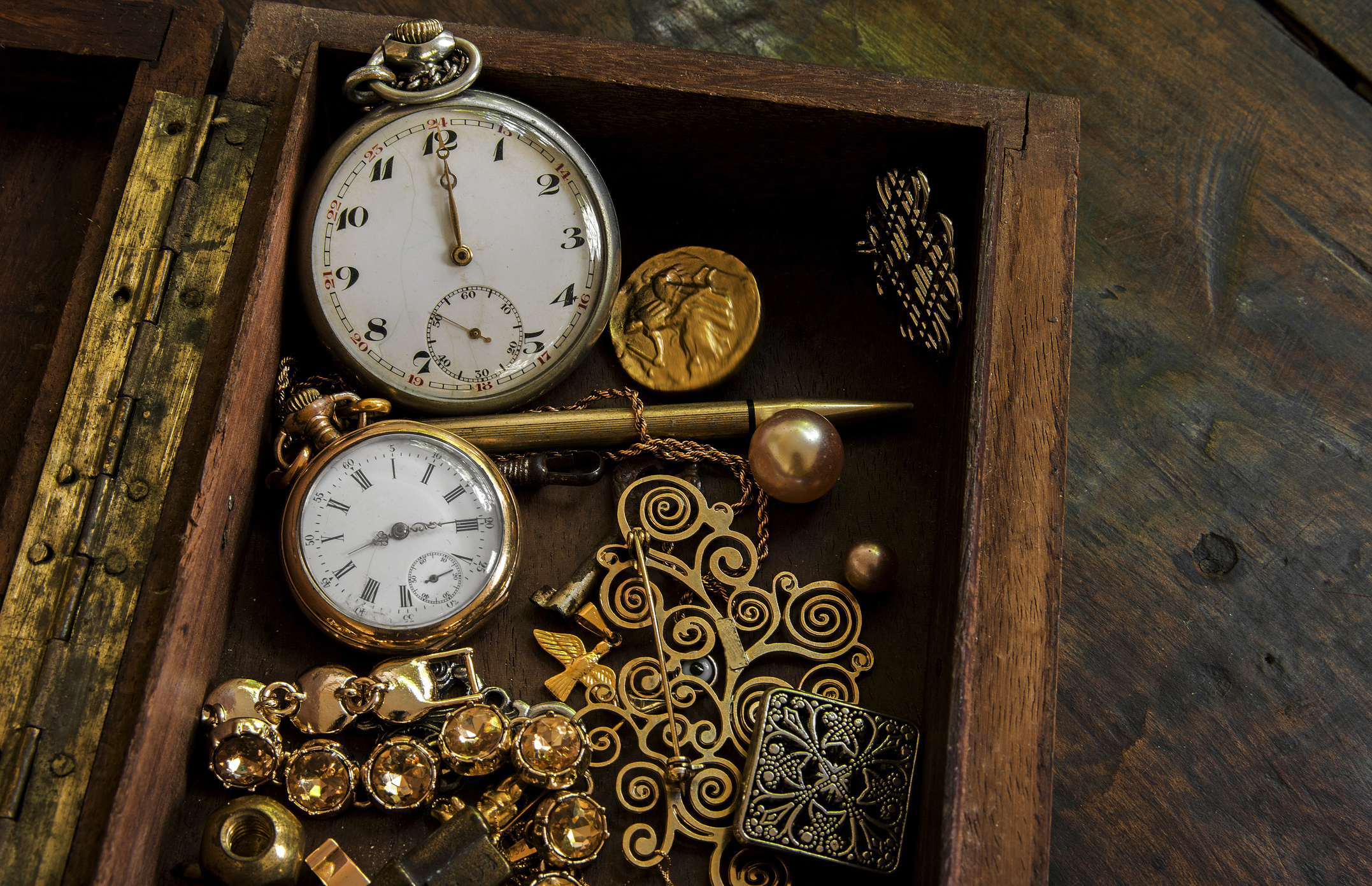 Old wooden box containing 2 antique pocket watches and many pieces of gold and silver. The history of the pocket watch begins in the 16th century with Peter Henlein in Germany, creating the first portable models, the &amp;quot;Nuremberg Eggs,&amp;quot; which were large and oval, serving more as jewelry and status symbols than precise instruments. Advances such as the anchor escapement (17th century) and mass production (19th century) increased accuracy and accessibility, making them popular among men until the rise of the wristwatch after World War I, when they became collector's items or retro accessories.