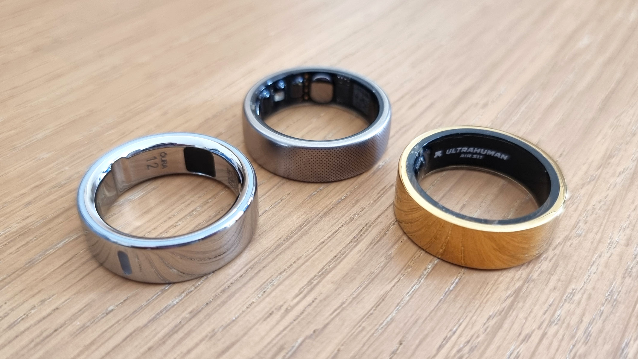 A close-up image of the Oura Ring Gen 4, Amazfit Helio and Ultrahuman Ring AIR smart rings lying flat on the table next to each other