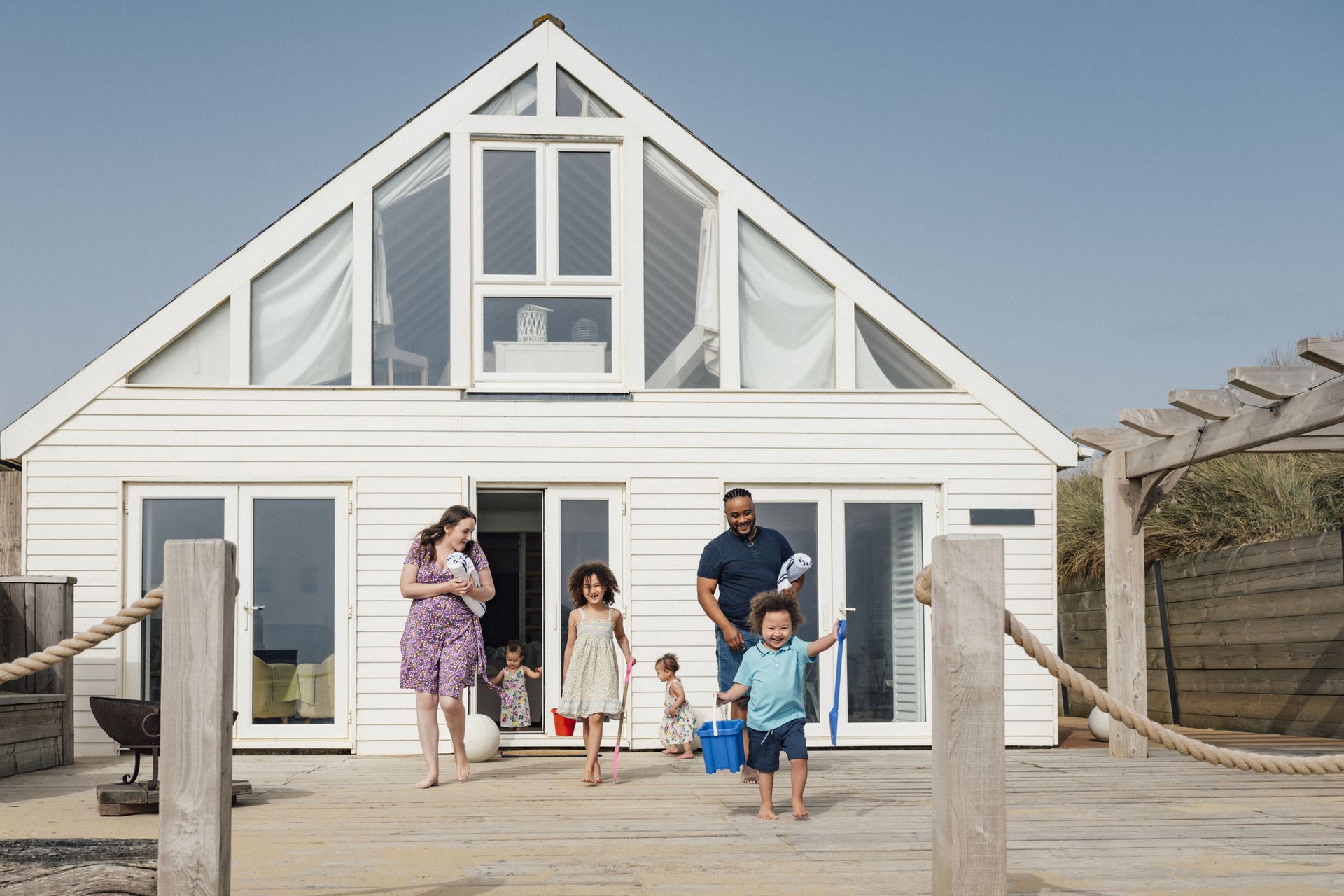 A couple with four children walks out of a vacation home across the deck to the beach.