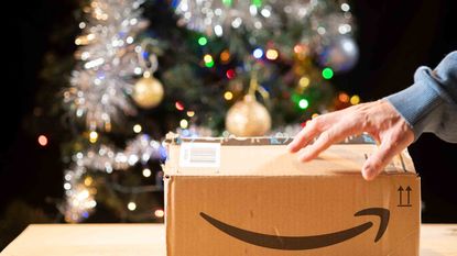 A hand on top of an Amazon box on a table in front of a Christmas tree