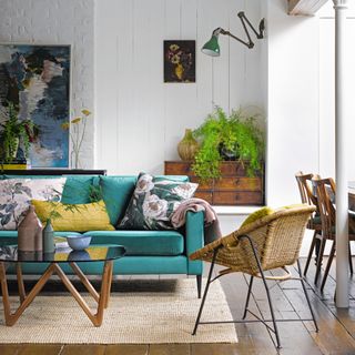 Blue velvet sofa with floral patterned cushions, rattan armchair, glass coffee table in white painted living room