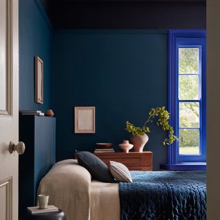 A bedroom colour drenched in navy paint with a cobalt blue window frame