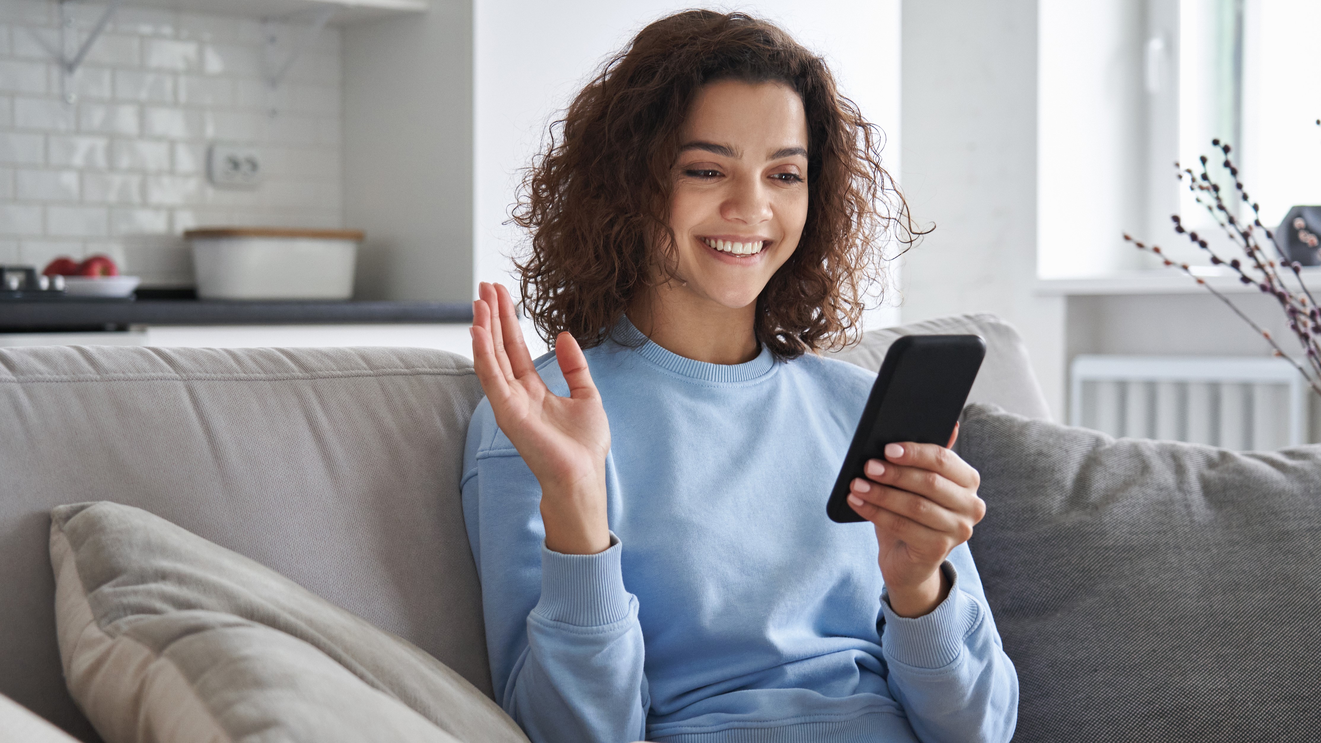 Woman smiling widely and looking at her phone, while holding her hand up