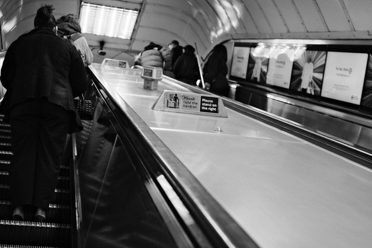 Black-and-white view up a London Underground escalator with commuters