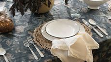 Black floral tablecloth with raffia placemats, white crockery, cream lace-trimmed napkins and silver flatware
