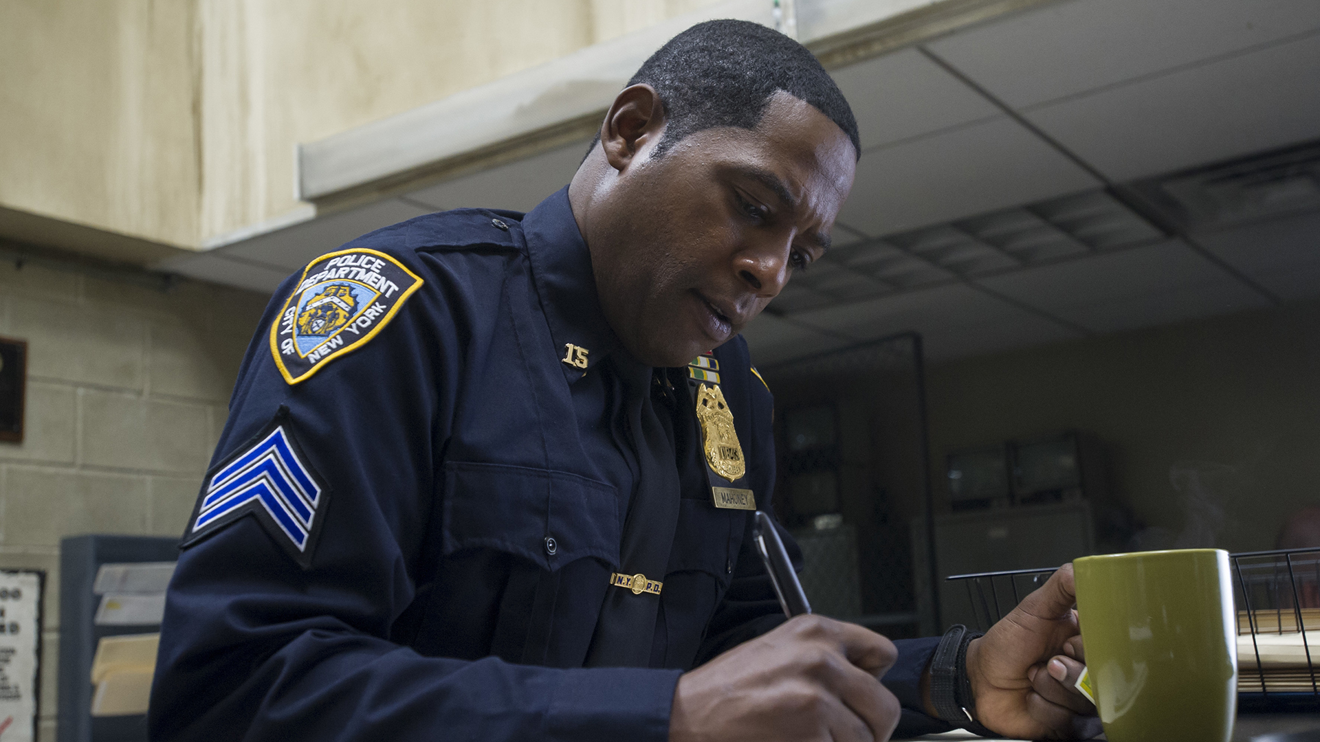 Brett Mahoney filling in a form with a pen and holding a cup of coffee in Netflix's Daredevil TV show