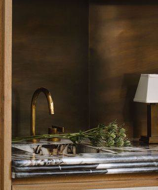 A marble countertop and gold sink with a small lamp and bouquet of flowers